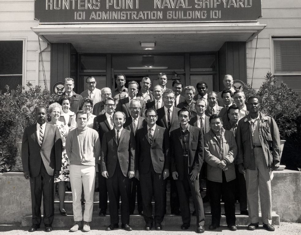 Group posing in front of Hunters Point Naval Shipyard Administration Building, 1970.