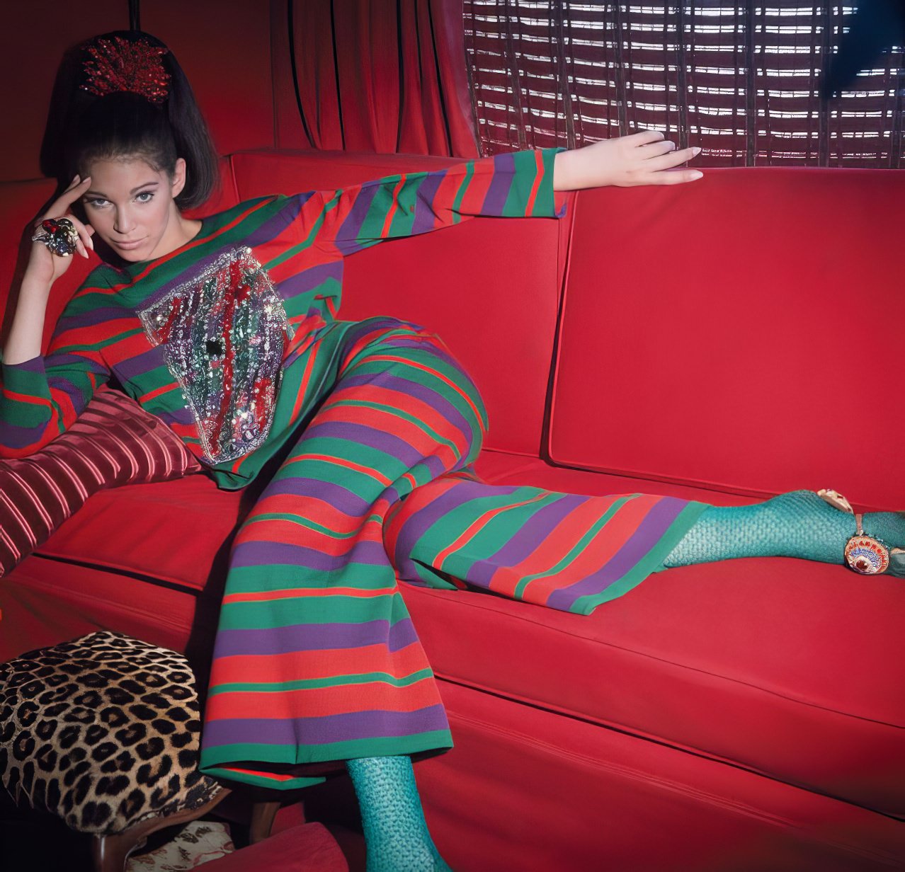 Ann Turkel wearing striped dinner pajamas by Galanos on a red couch, 1966.