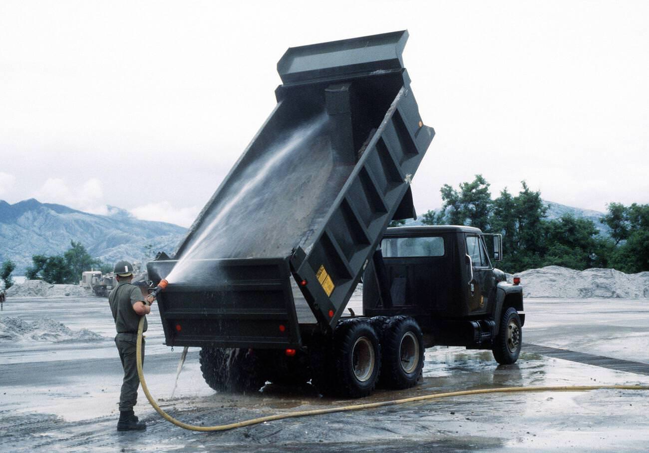 A Seabee hoses a dump truck used in the cleanup of volcanic ash at Naval Air Station Cubi Point, Luzon, Philippines, after Mount Pinatubo's eruption.