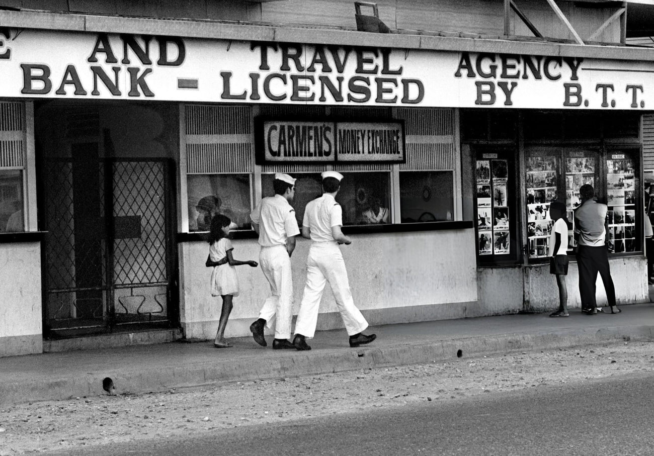 In Olongapo, Philippines, 1972, a Filipino girl asks U.S. Navy sailors for money near a money exchange business, highlighting the city's popularity among sailors from the U.S. Naval Base Subic Bay.