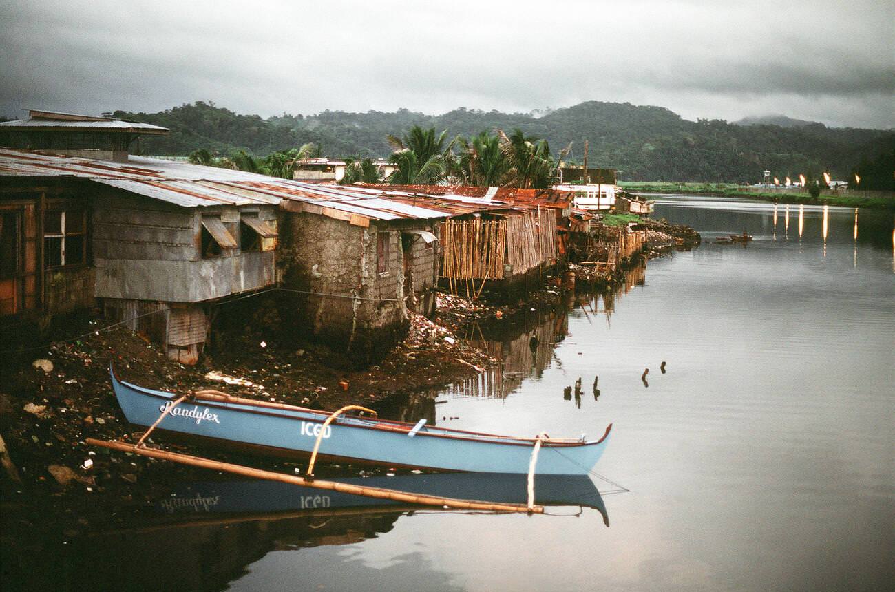 Poverty-stricken houses along a riverbank at sunset, 1981.