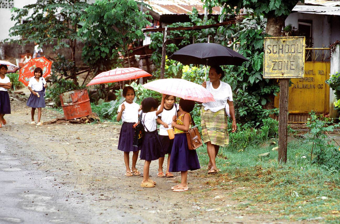 Children with umbrellas waiting for a school bus, 1981.