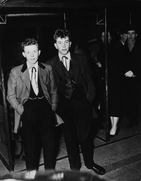 Two original 1954 Teddy Boys at Kingston upon Thames wearing Drape Jackets with 4″ wide lapels, silk patterned waistcoats and trousers with pleated fronts and 16″ bottoms with turn-ups.
