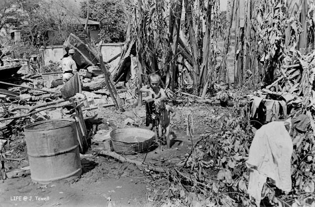 Older Filipino woman giving a child a bath by the ruins of her home, Manila, Philippines, March 1945