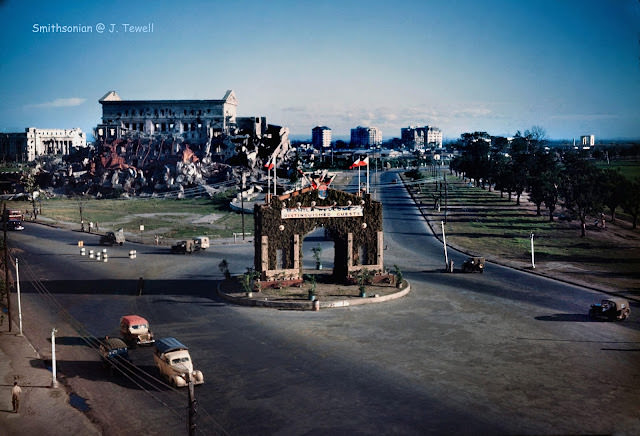An arch with the sign ‘Manila Welcomes Distinguished Guests’ in a traffic circle in Manila, the Philippines, 1945. The photo was taken from Manila City Hall looking south-southwest down Padre Burgos Ave.