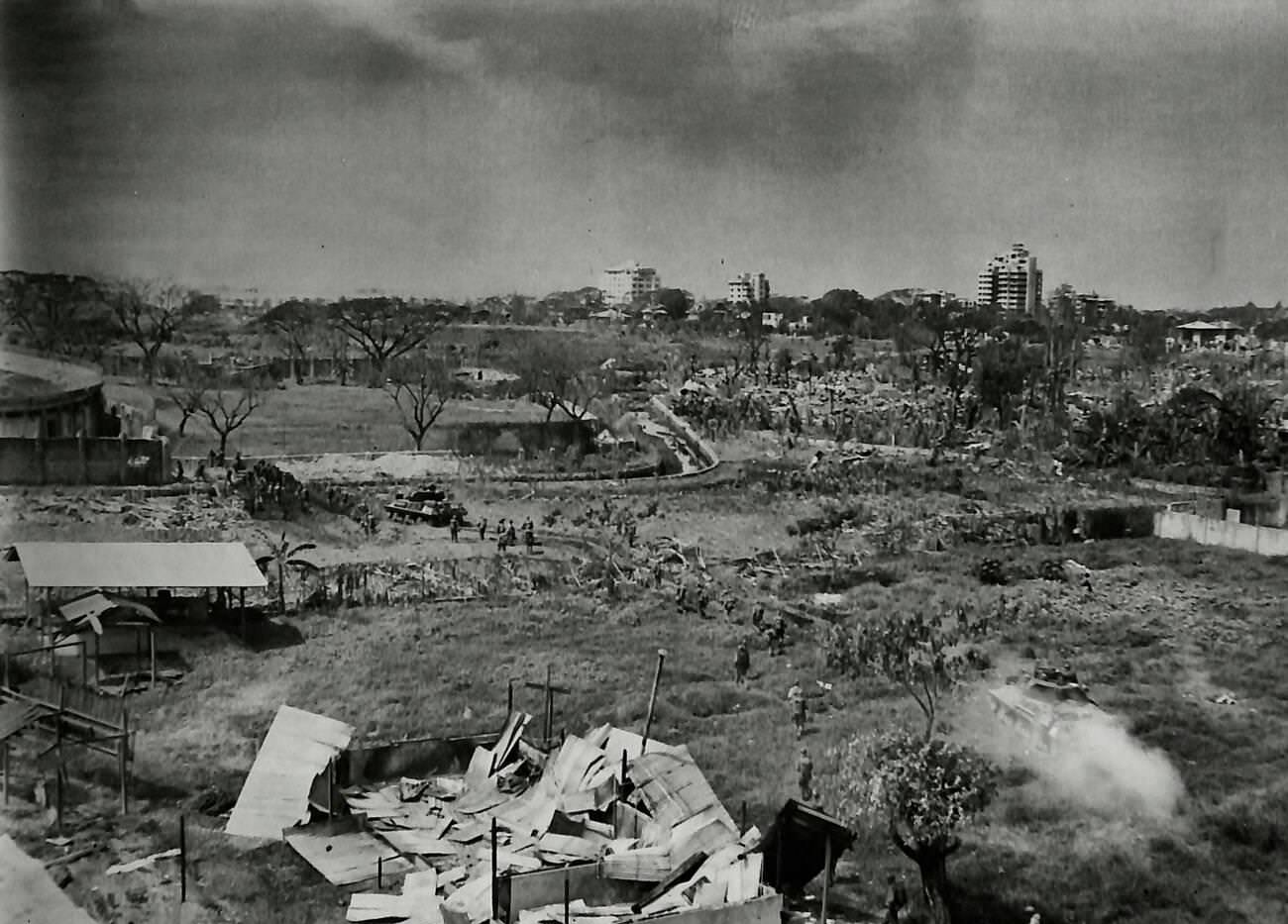 From La Salle Girls College's roof, tanks approach a football field behind Rizal Stadium in Manila, overcoming a moat barrier with an American bulldozer, 1945.