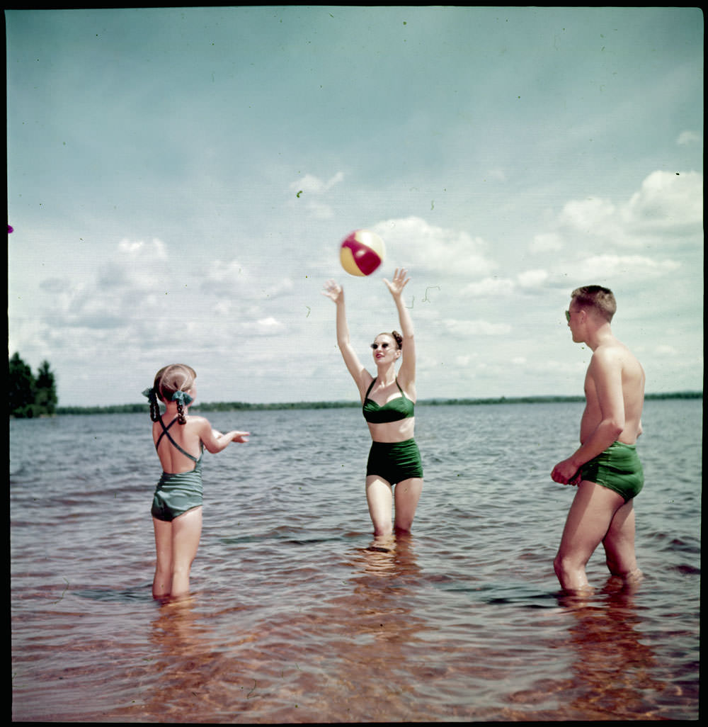 Man, woman and young girl playing with a beach ball in the water at the beach, 1950
