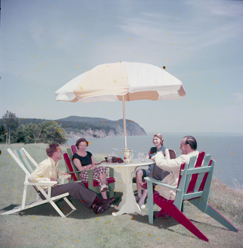 Two men and two women have drinks under an umbrella at an outdoor table, Fundy National Park, New Brunswick