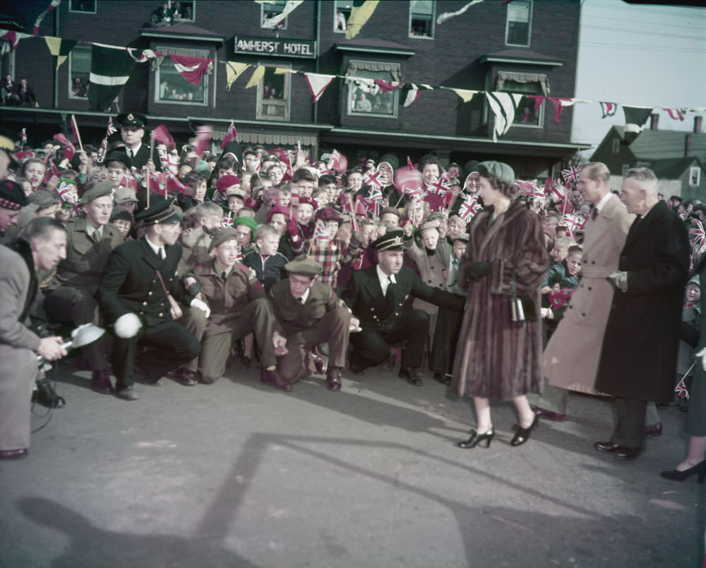 Queen Elizabeth II, Prince Phillip and another elderly man stand before a crowd of spectators, 1951