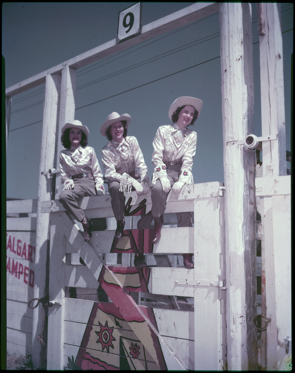 Mrs. Merle K. Stier, Stampede Queen (centre), and two attendants watch riding and roping events at the Calgary Stampede