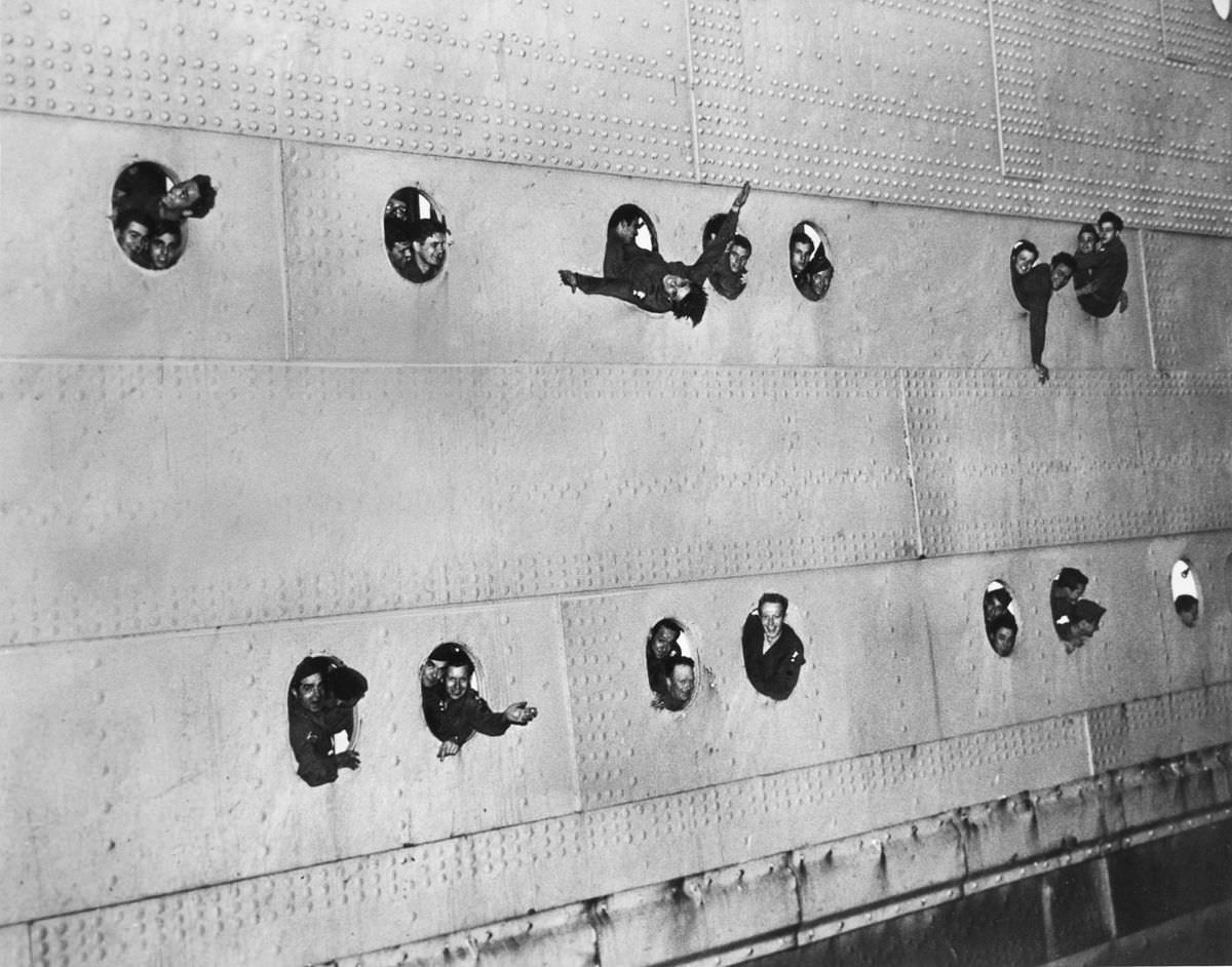 Military personnel wave from the portholes of a ship, 1945.