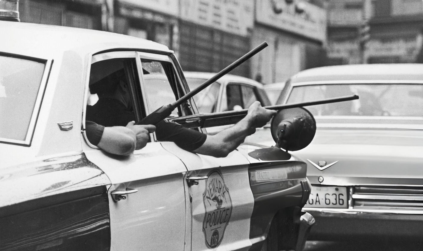 Police officers hold rifles out of the windows of a police cruiser on Springfield Avenue