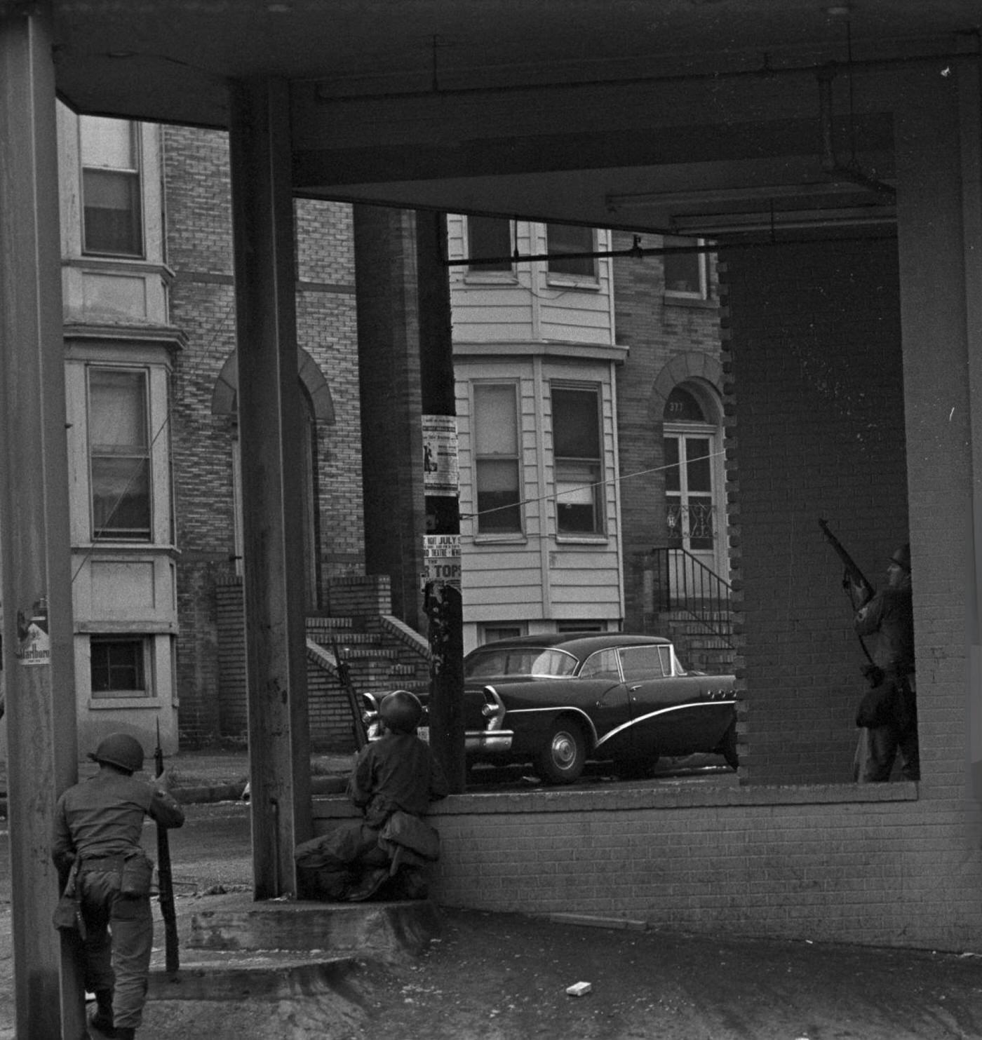 National Guard soldiers taking cover under the awning of a building, guns pointed towards the street