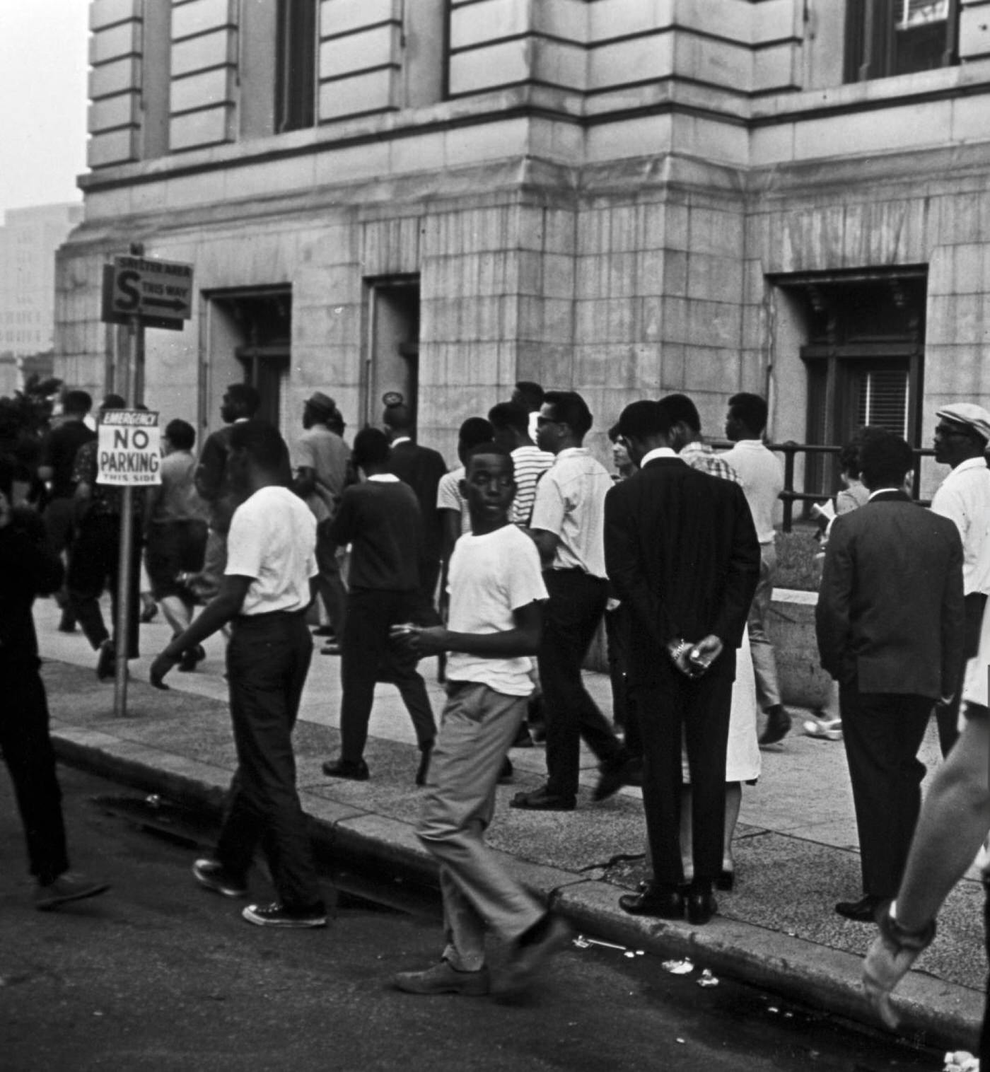 A group of residents disperses under the direction of armed police officers on a sidewalk