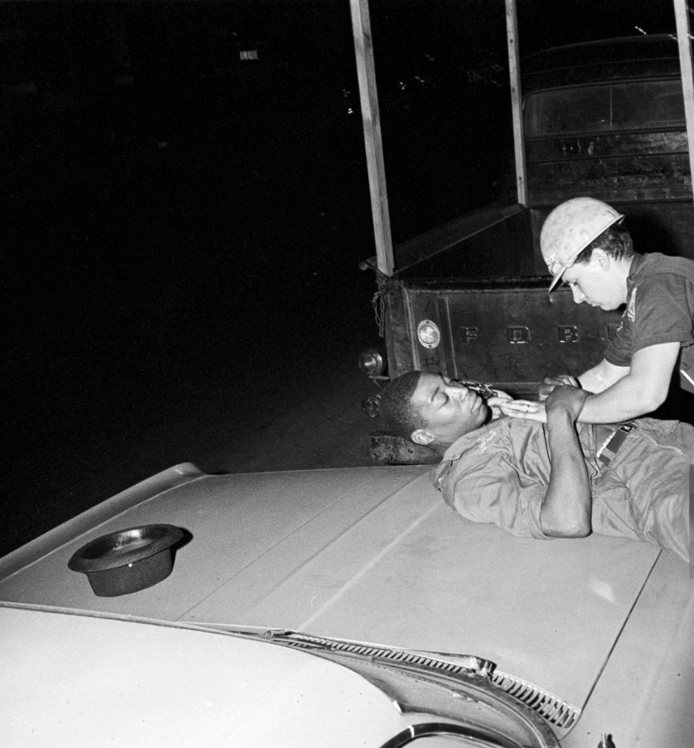 A young African-American man lying on the hood of a parked car is searched by a group of National Police officers