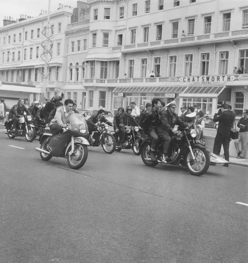 A lone mod drives his scooter up alongside a group of rockers in Hastings, England, 1964.