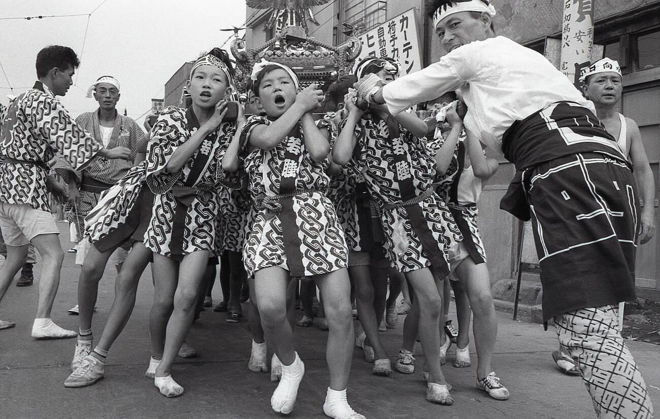 Boys in happy coats heave a mikoshi, a portable Shinto shrine, at a matsuri in Tengenji, Tokyo, 1958.
