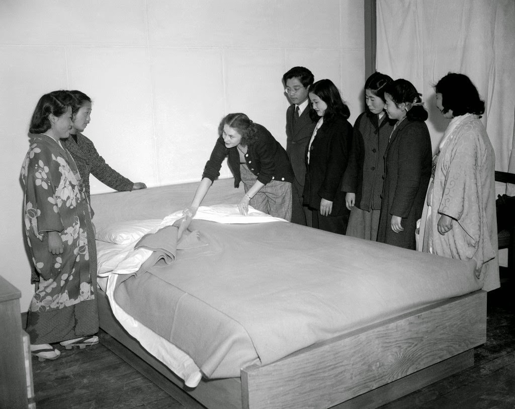 Although given preliminary instructions the girls are a bit vague about the proper making of a bed. Mrs. Anderson, with the help of an interpreter attached to the liaison section for the housing development, demonstrates the American way of bed making in Tokyo, 1947.