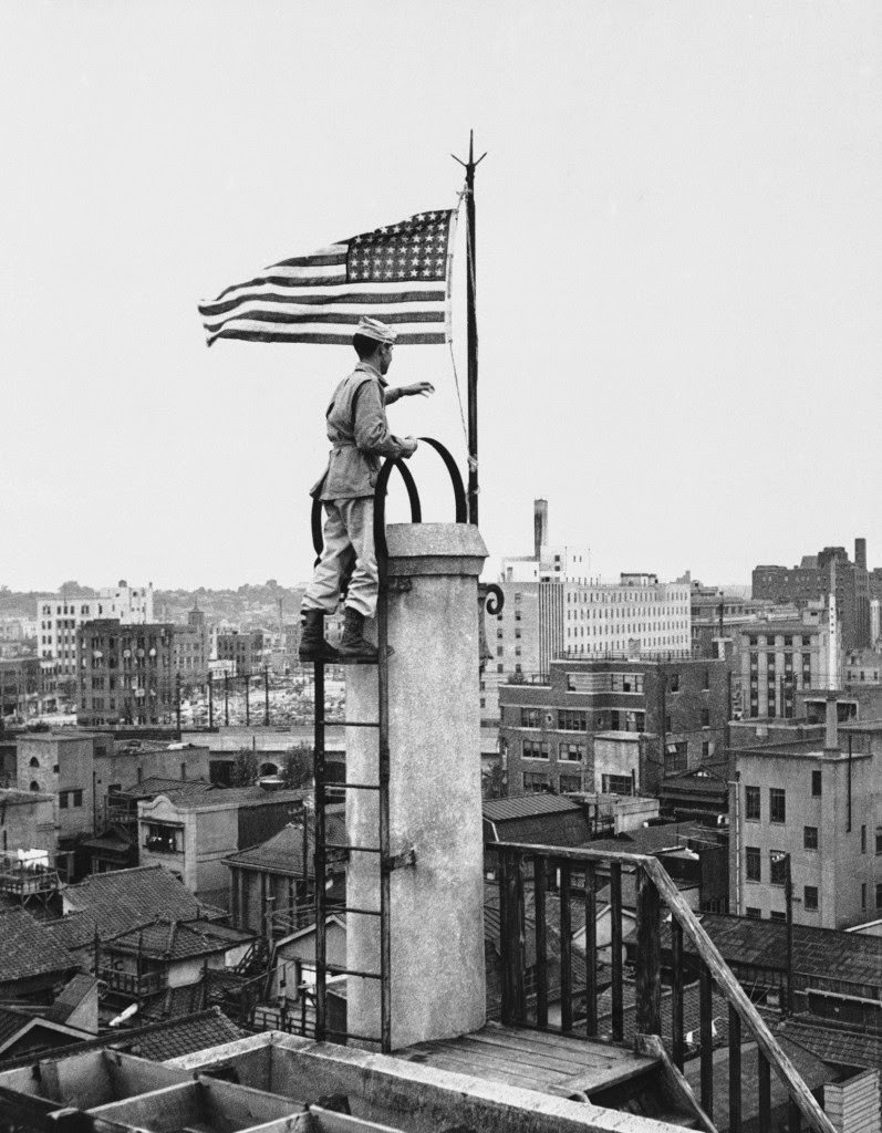 The American flag, first to fly over Tokyo since the Japanese surrender, is raised over the Nippon News building in downtown Tokyo by Lt. Bud Stapleton of Syracuse, New York, 1945.