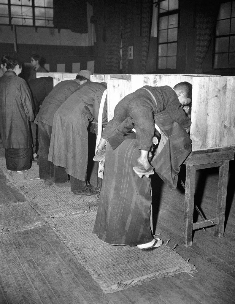 A Japanese woman carries her son on her back as she marks her ballot in Tokyo, 1946.
