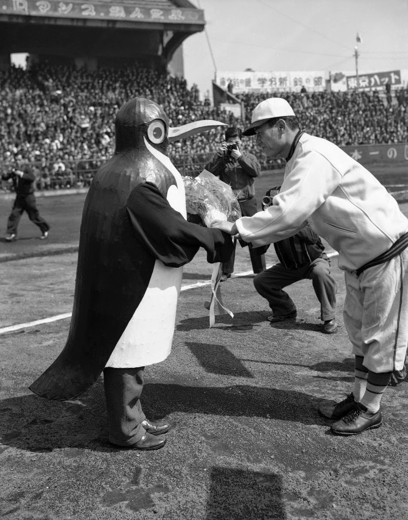 As the baseball season opened in Japan, a penguin-costumed attendant presents flowers to the manager of one of the eight teams in the league in Tokyo, 1949.