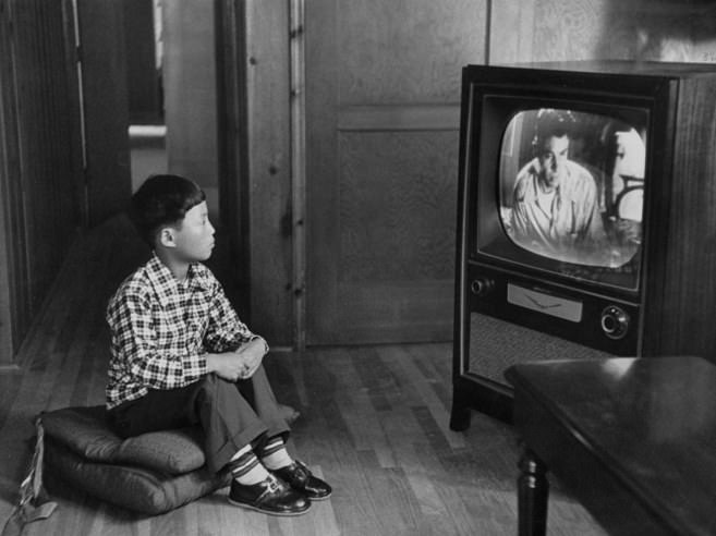 An adopted Korean war orphan, Kang Koo Ri, watches television in his new home in Los Angeles in 1956