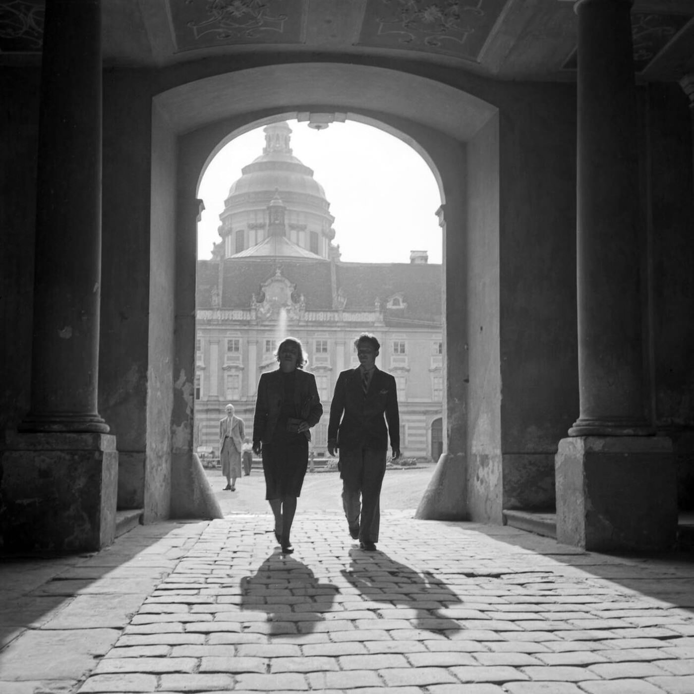A man and woman walking through Melk Abbey's archway, Austria, 1930s.