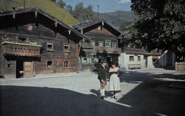 A man and woman standing in the sun on a Wagrain street corner, Austria, 1929.