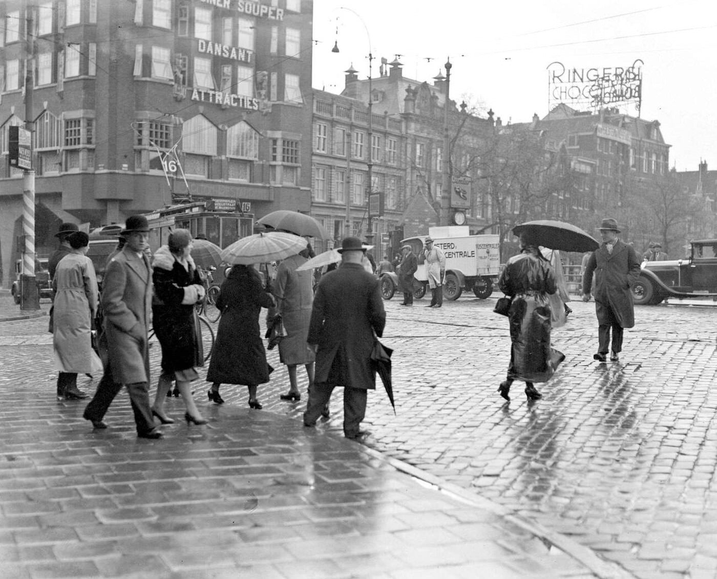 Pedestrians cross the street at the Munt in a rainy Amsterdam, 1930s.