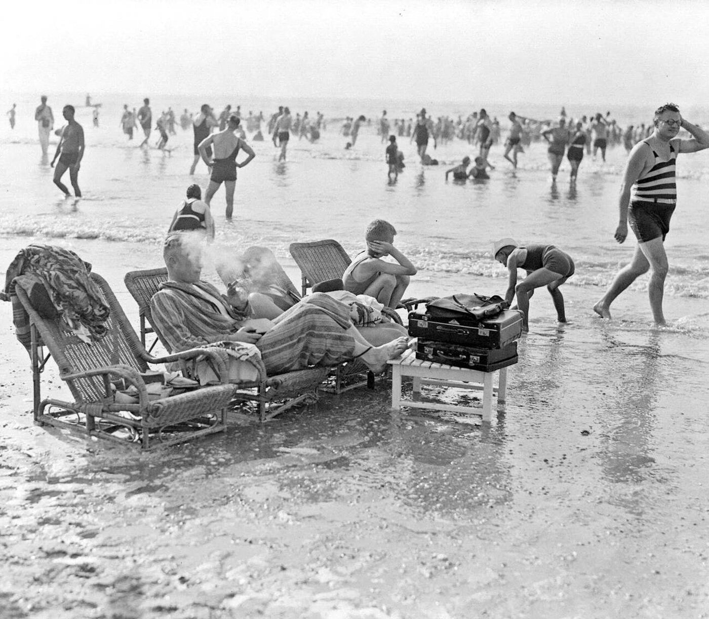 Bathers sitting on wicker loungers in the sea at the beach, 1930s.