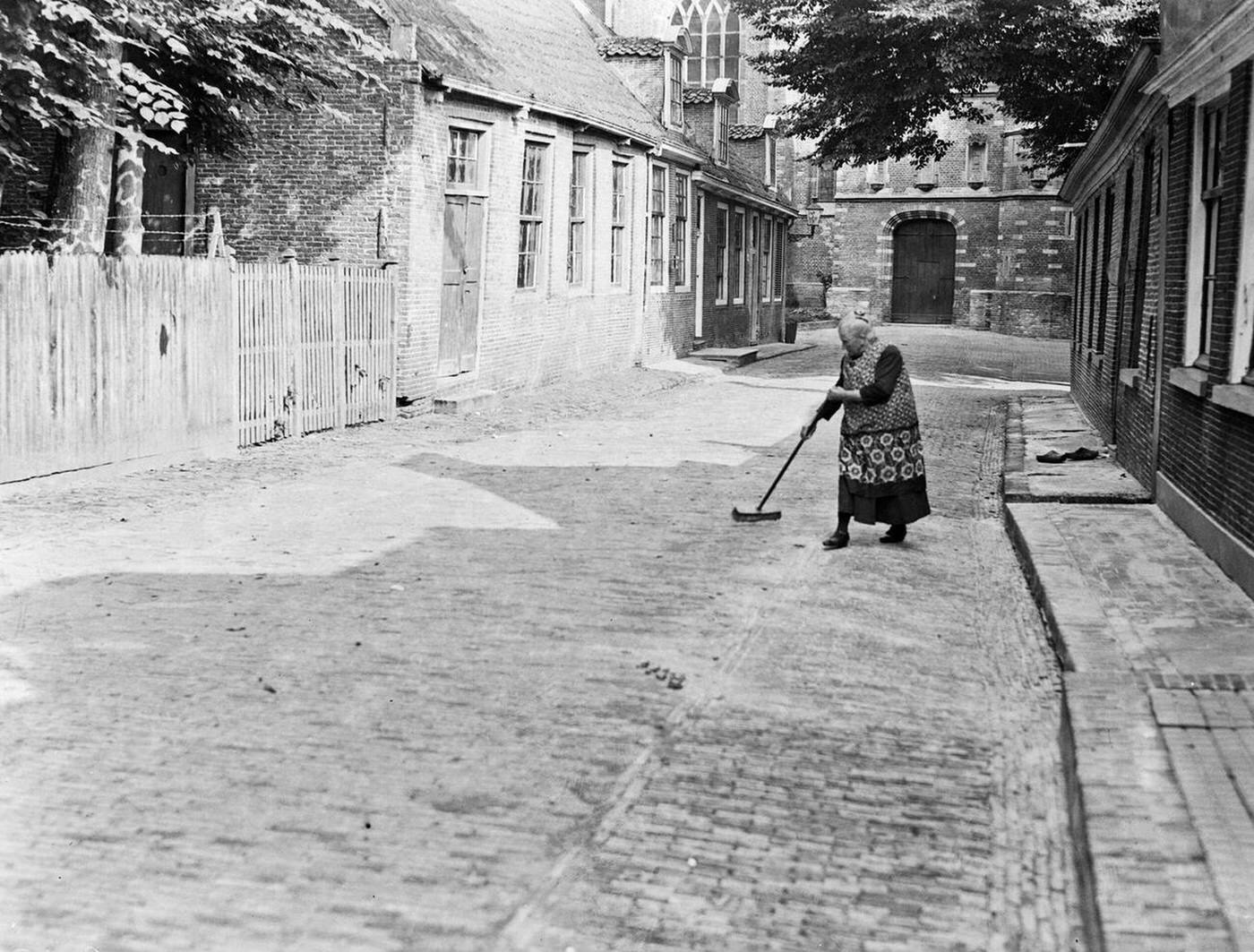 Street in Edam with a sweeping woman and a church in the background, 1930s.