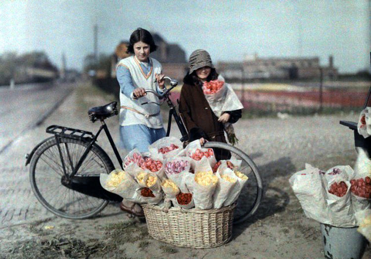 Two young girls stand near flowers being sold on the side of the road in Haarlem, 1930s.