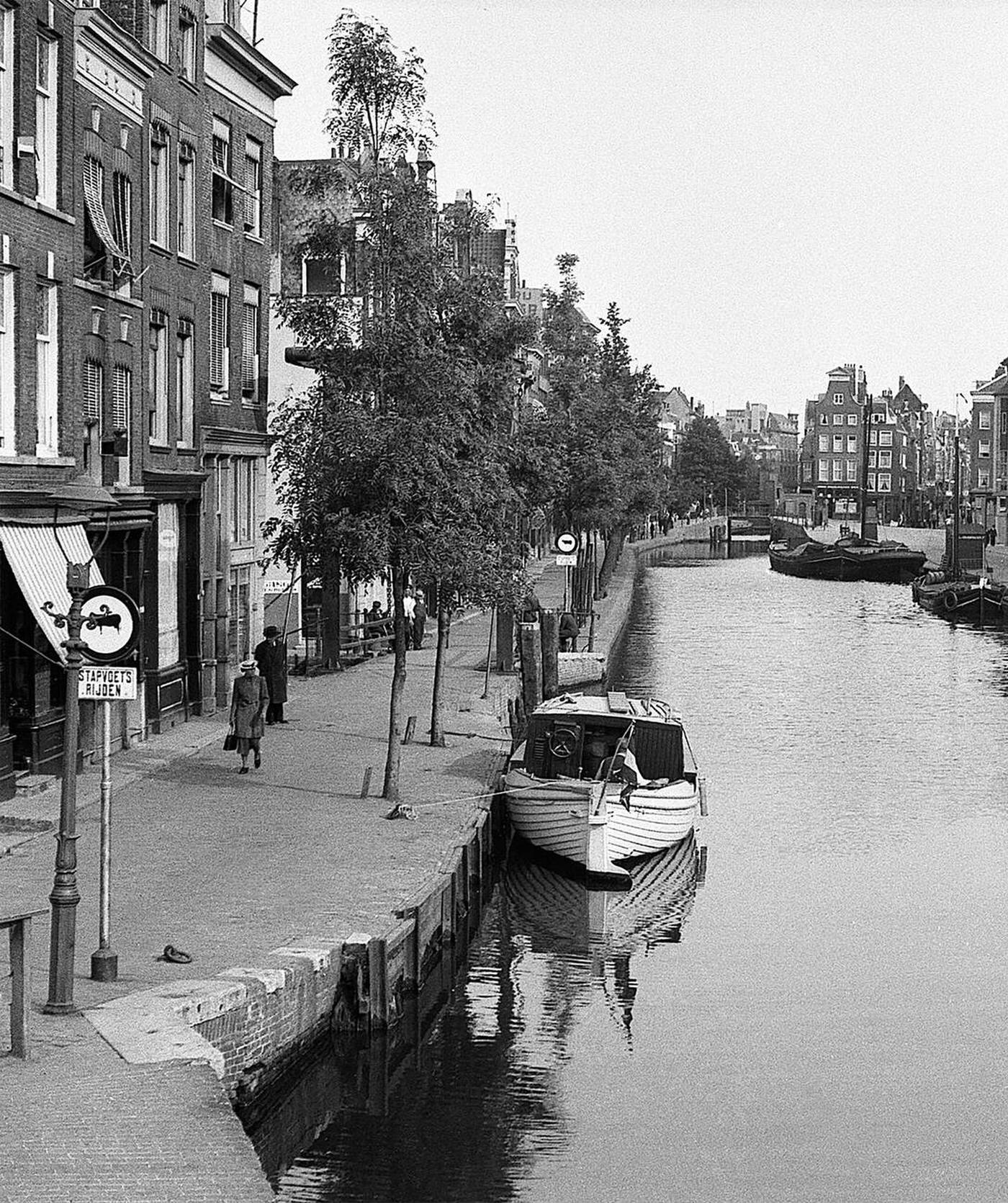 Canal-side scene in Amsterdam, Holland, with pedestrians and barges, 1930s.