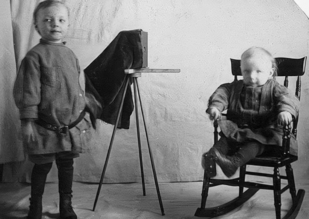This trimmed amateur photograph is not identified. The tripod appears to be homemade but the camera under the darkcloth is a real box camera.
