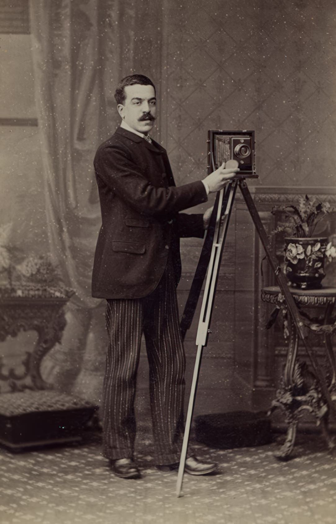 This cabinet card shows a mustached man with a folding camera in a studio setting.