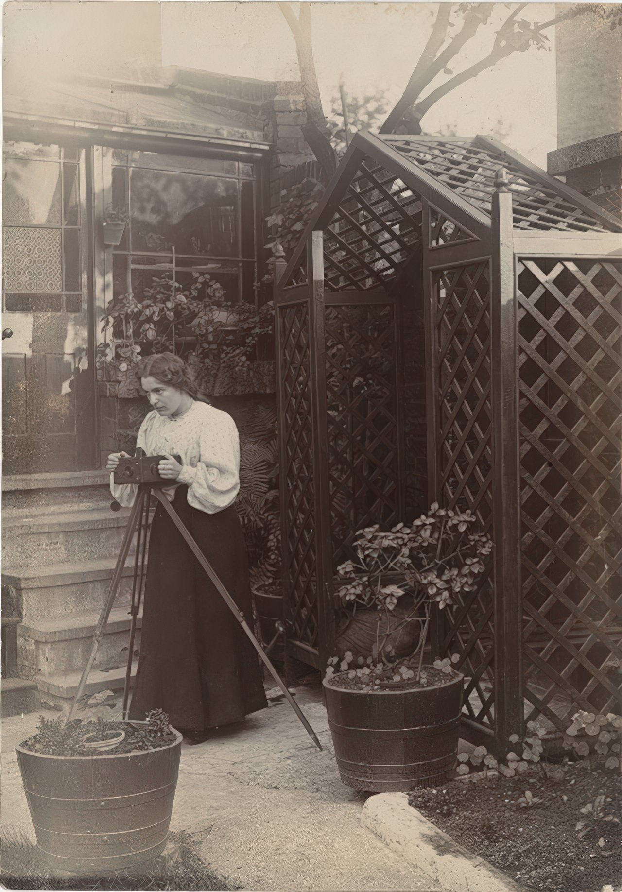 Young woman is standing behind a camera on a tripod in a back garden.