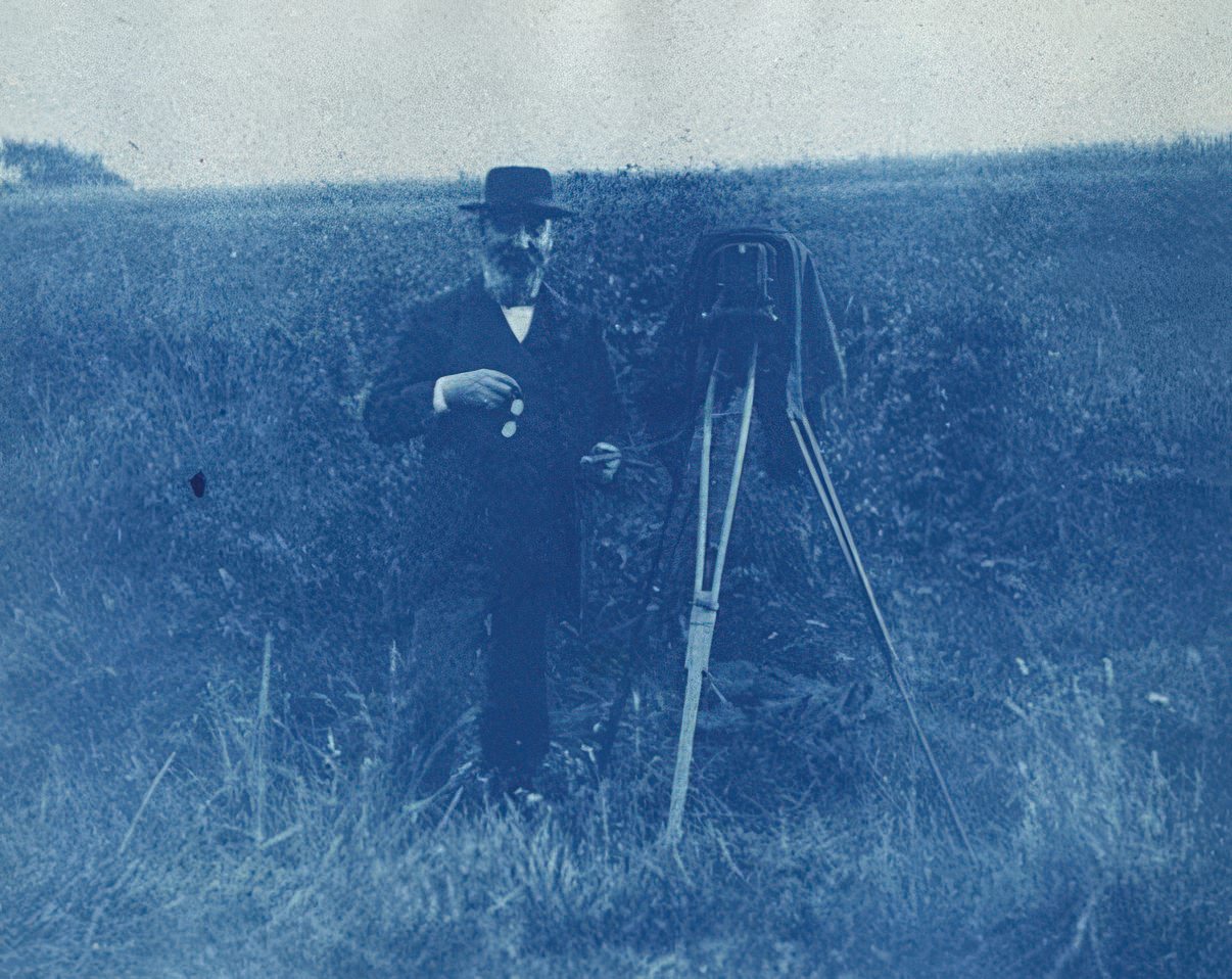 Cyanotype of a photographer with a cable release in his hand in a field, 1893.