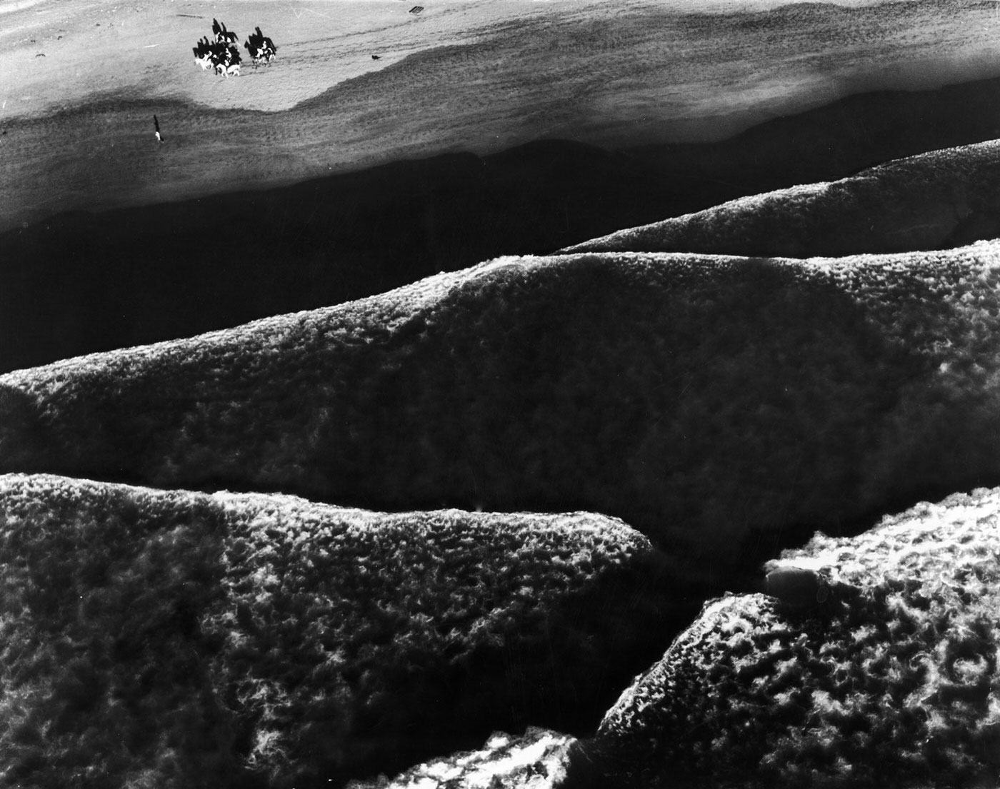 Beach riders guide their horses along the shore at high tide at Ocean Beach, near Fort Funston, California, as the long, low Pacific rollers make mountain like patterns of the surf.