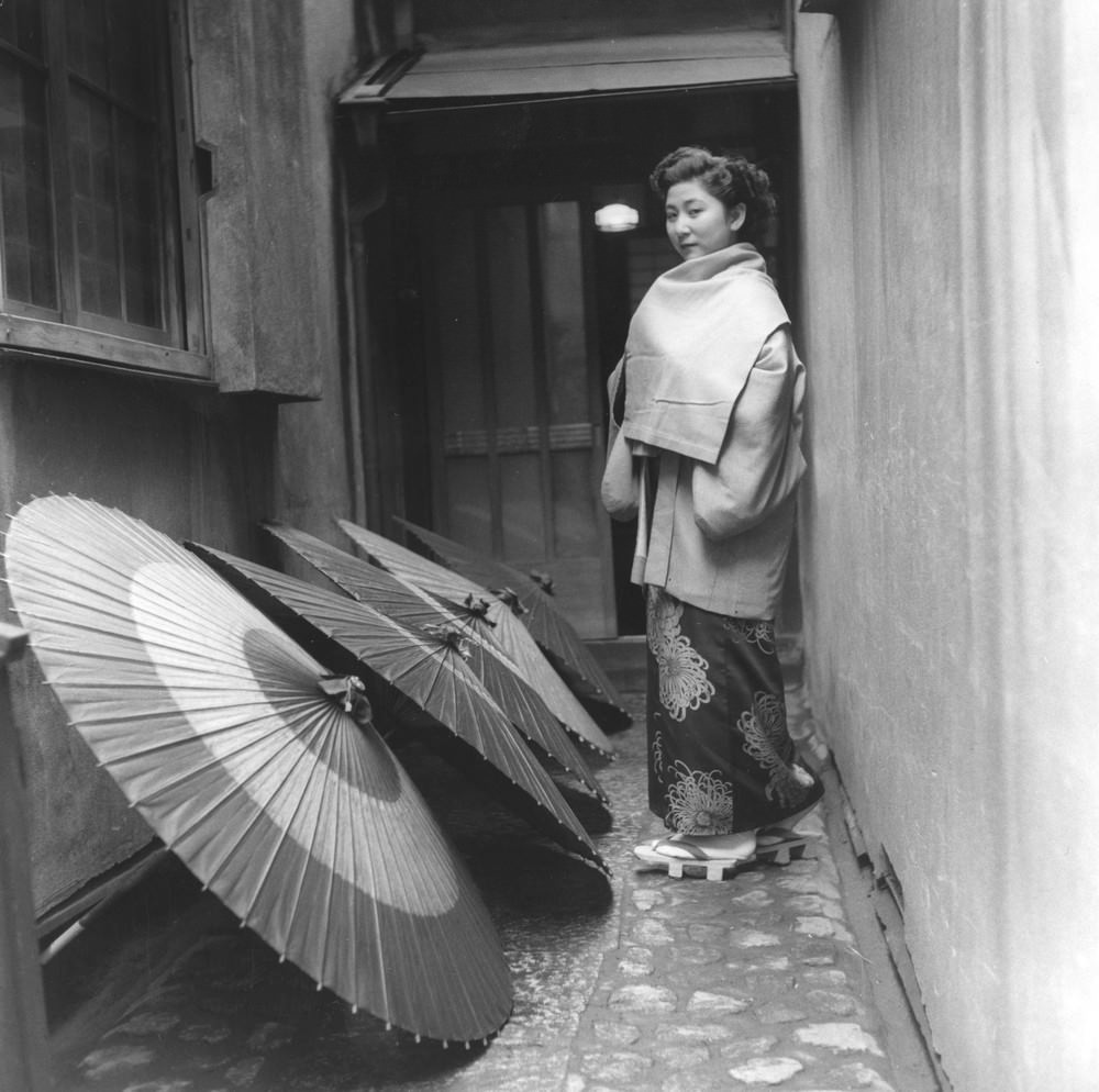 A Geisha passing drying umbrellas, 1950s.