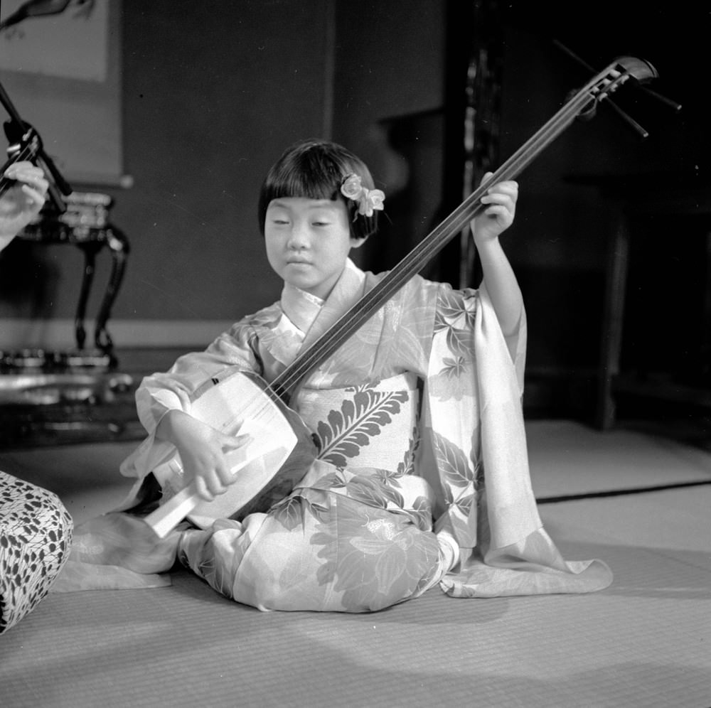 A young girl in a geisha kimono playing the samisen, 1950s.