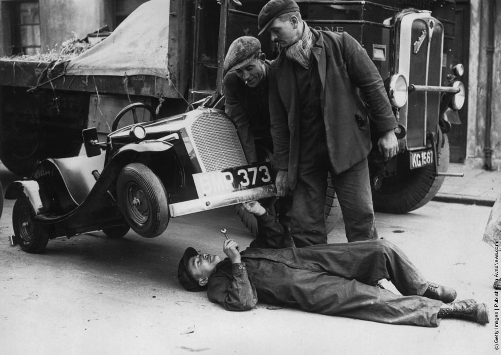 Instead of using a car jack to carry out repairs on a one horsepower midget car, a mechanic in Cardiff simply gets a couple of helping hands to lift up the front of the vehicle. Midget cars are on sale for around £70 and achieve a top speed of about 50 miles per hour. 11th February 1935.