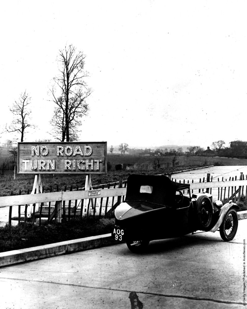 A three-wheeled car passes a sign where the London North Orbital road will be constructed at West Hyde Lodge near Rickmansworth. 22nd February 1935.