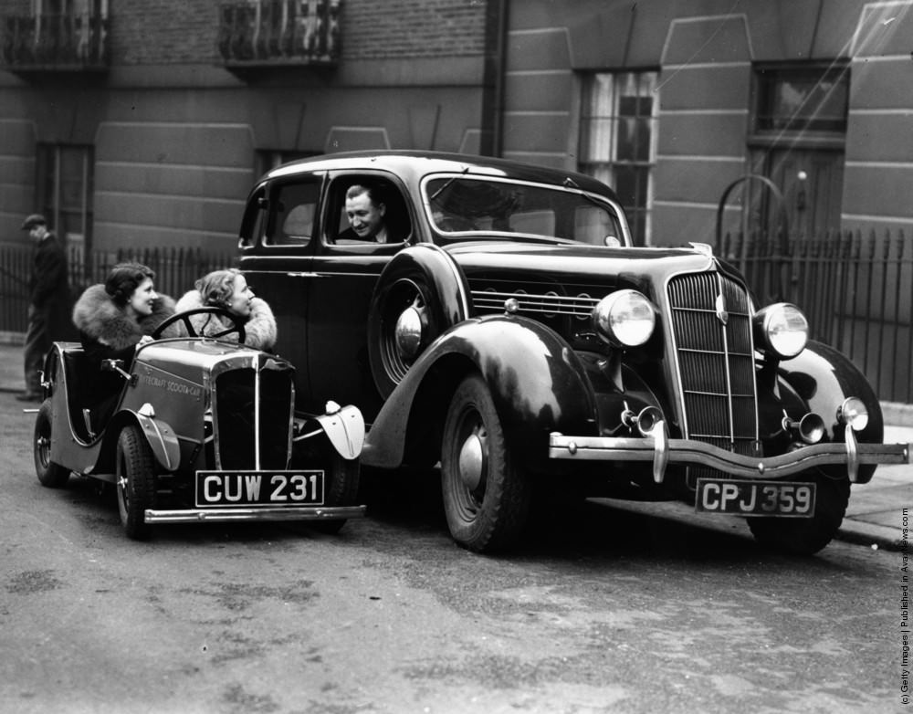 Two women sit in a newly-designed 2 1/2 hp Scoota car, made by the British Motor-Boat Manufacturing Company, at demonstrations at Britannia House. The little car, which can carry two people at speeds up to 45mph, is dwarfed by an ordinary-sized vehicle. 2nd April 1936.