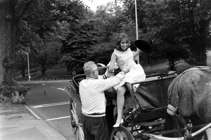 A young woman is helped down from a horse-drawn carriage, Central Park, 1961