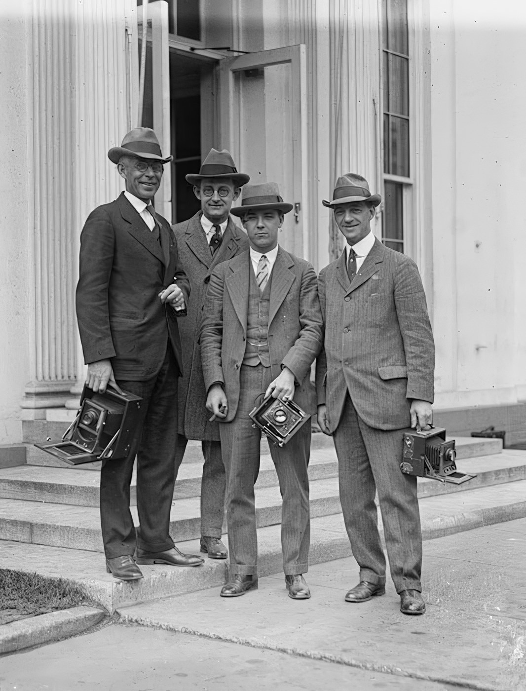A group of early-1900s photographers posing with their cameras on steps.