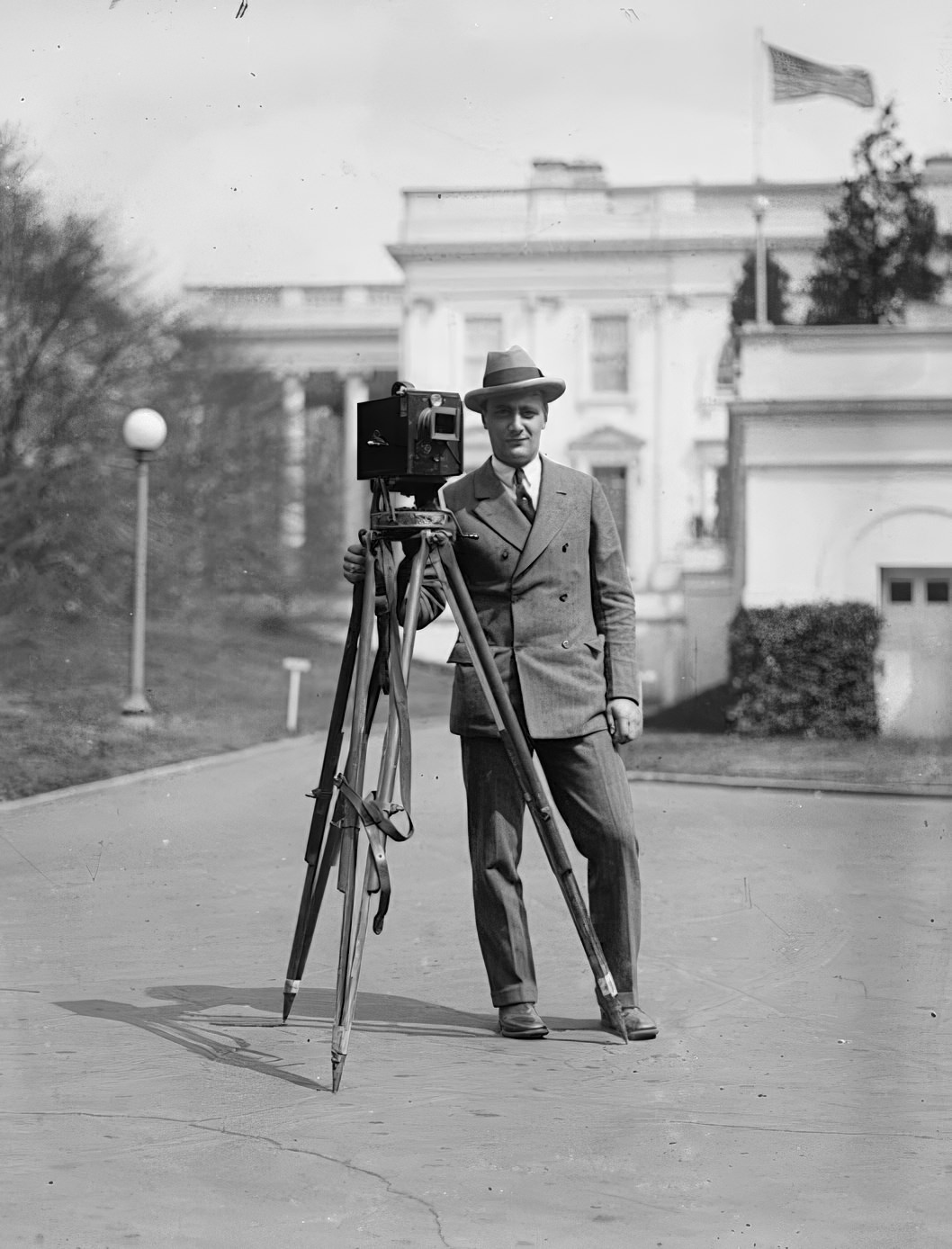 A photographer posing with his camera and tripod outside the White House in the early 1900s.