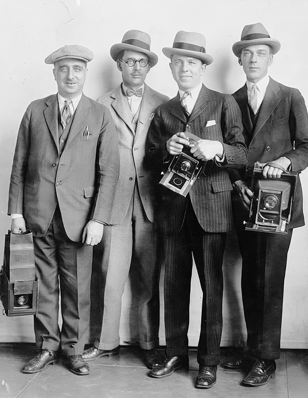 Group portrait of four members of the White House News Photographers' Association, standing, facing front, holding cameras, circa 1920s