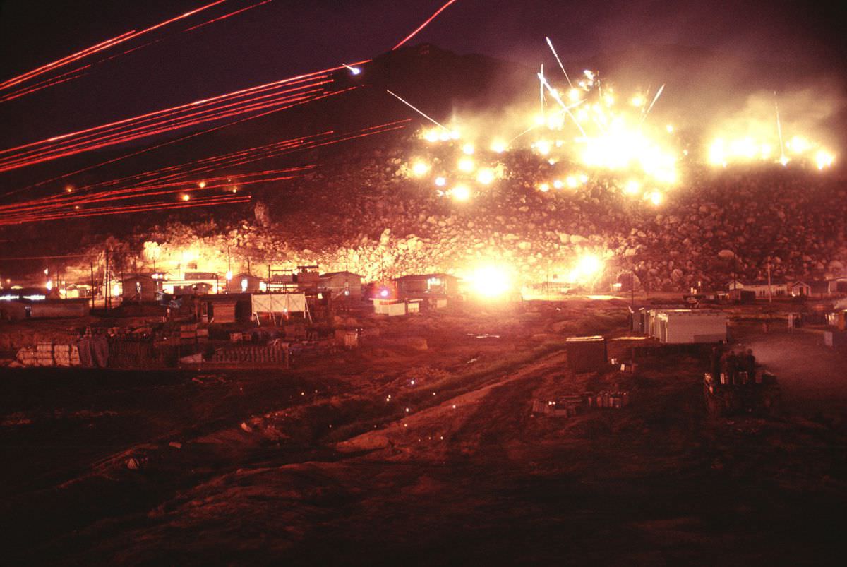 Hand-launched flares illuminate the hills as soldiers fire M60 machine guns with red tracers. One round can be seen ricocheting near the top of the mountain.