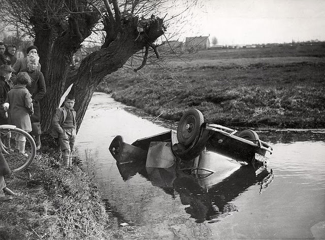 Bystanders near an upended car after it crashed into the water in the Netherlands, 1930s.