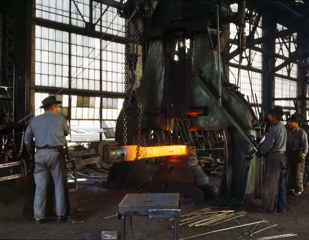 March 1943. “Santa Fe R.R. shops, Albuquerque. Hammering out a drawbar on the steam drop hammer in the blacksmith shop.” 4×5 Kodachrome transparency by Jack Delano for the Office of War Information.